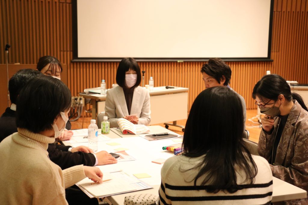 白い長机を囲んで石川さんと参加者6名が対話をしている様子。