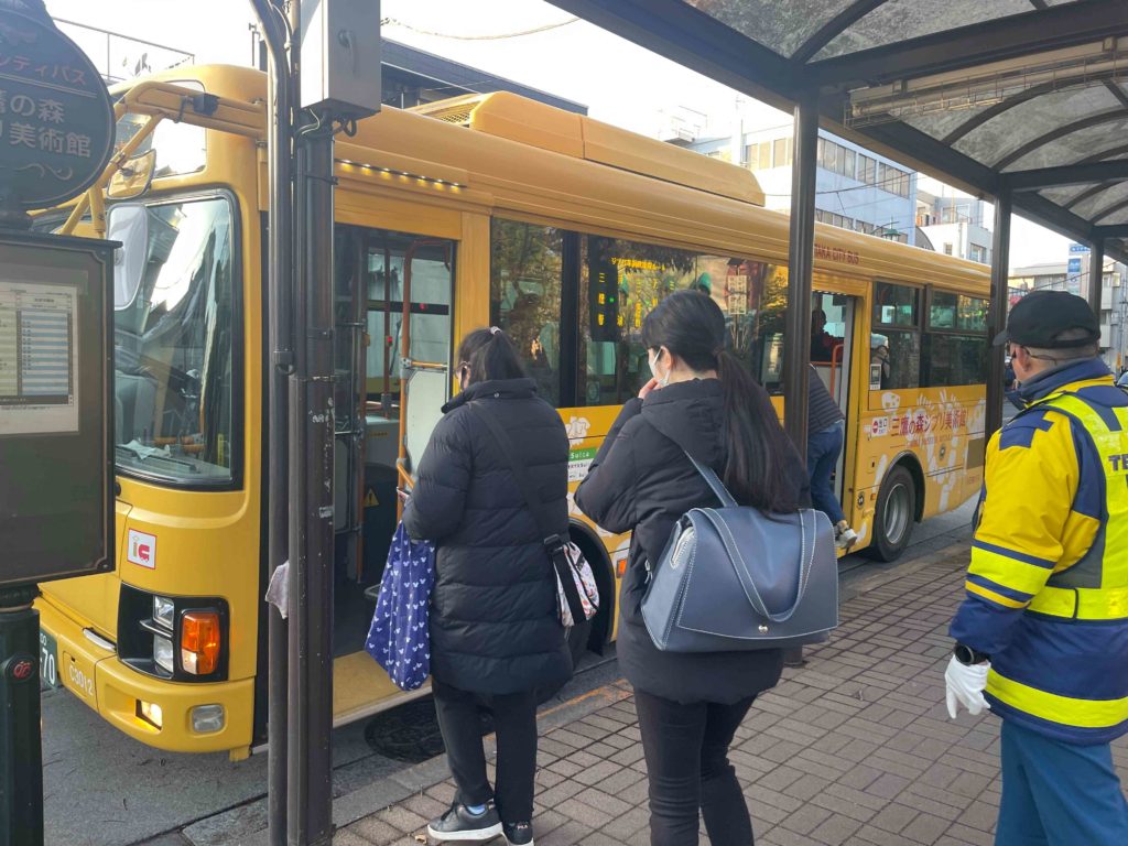 バス停に停止する黄色いコミュニティバスに乗り込む様子。